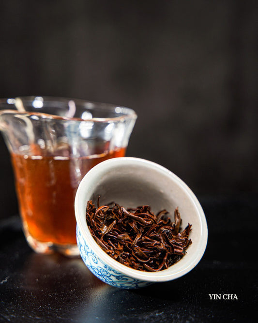 Dianhong black tea leaves in a white ceramic bowl with a glass of brewed tea, Yin Cha branding