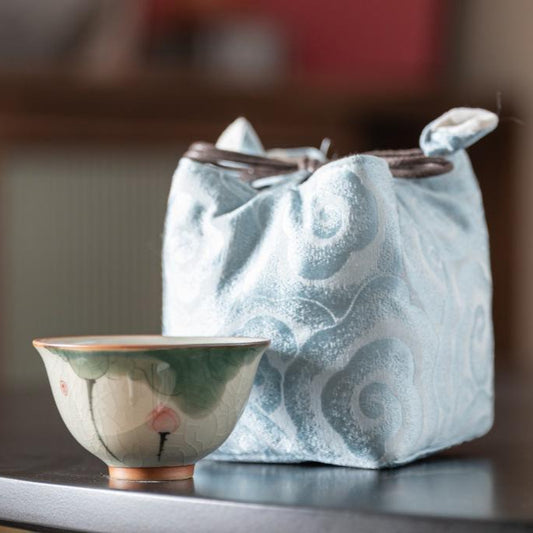 Dehua porcelain teacup with lotus design, shown with a blue silk gift bag.