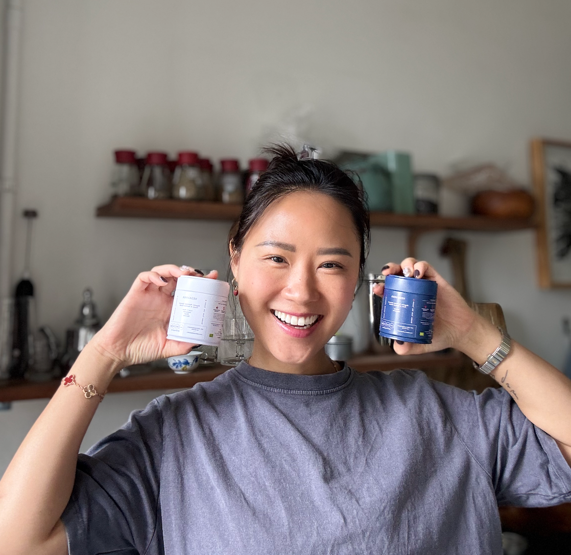 Woman holding two adaptogen blends, one white and one blue, in a kitchen setting.