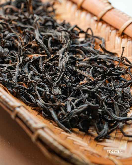 Loose Dianhong black tea leaves in a woven basket with Yin Cha branding