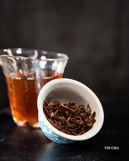 Dianhong black tea leaves in a white ceramic bowl with a glass of brewed tea, Yin Cha branding