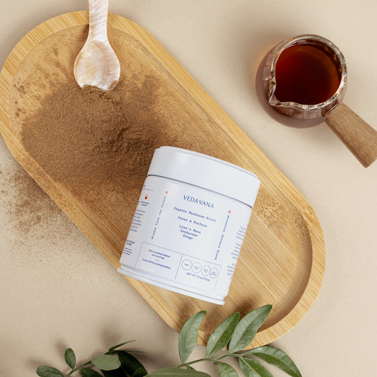 Vedavana organic mushroom extract powder with white container, tea, and scoop on beige surface