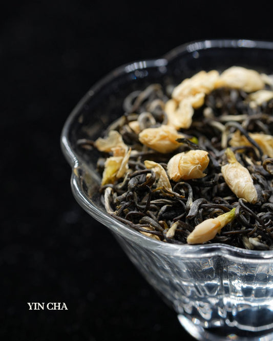Jasmine Ballet tea with golden flower petals in a glass bowl on black background