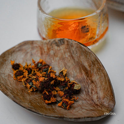 Dried Snow Chrysanthemum flowers on a wooden plate with a glass of brewed tea in the background
