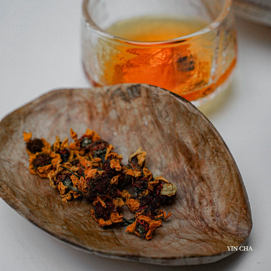 Dried Snow Chrysanthemum flowers on a wooden plate with a glass of brewed tea in the background