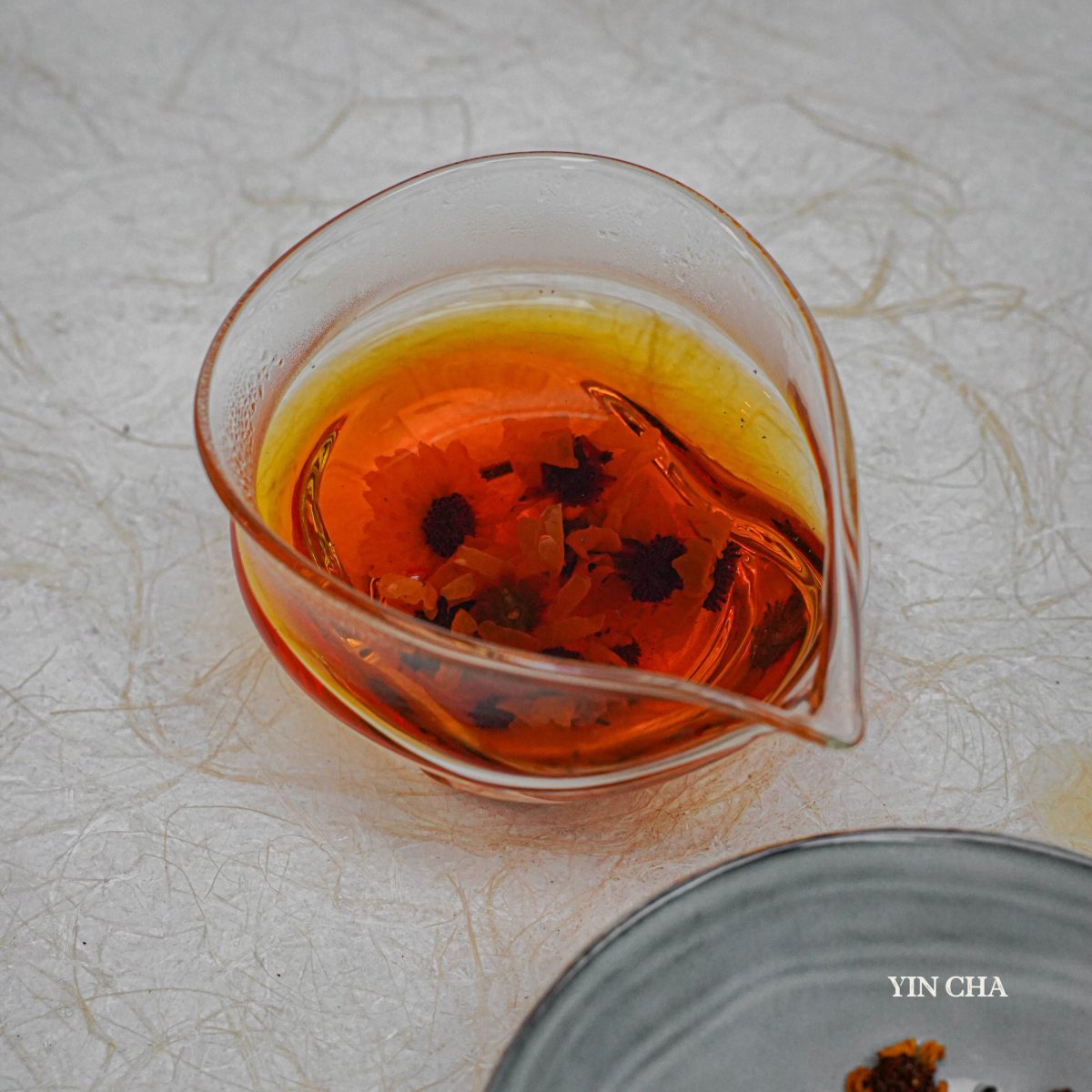 Brewed Snow Chrysanthemum tea in a glass teapot on a textured white background