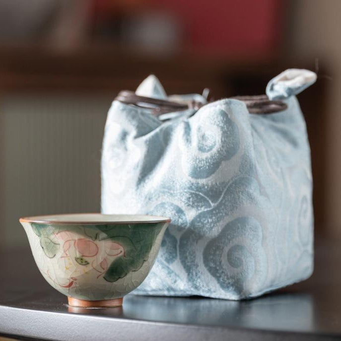 Ge Kiln style porcelain teacup with floral design next to blue patterned fabric bag.